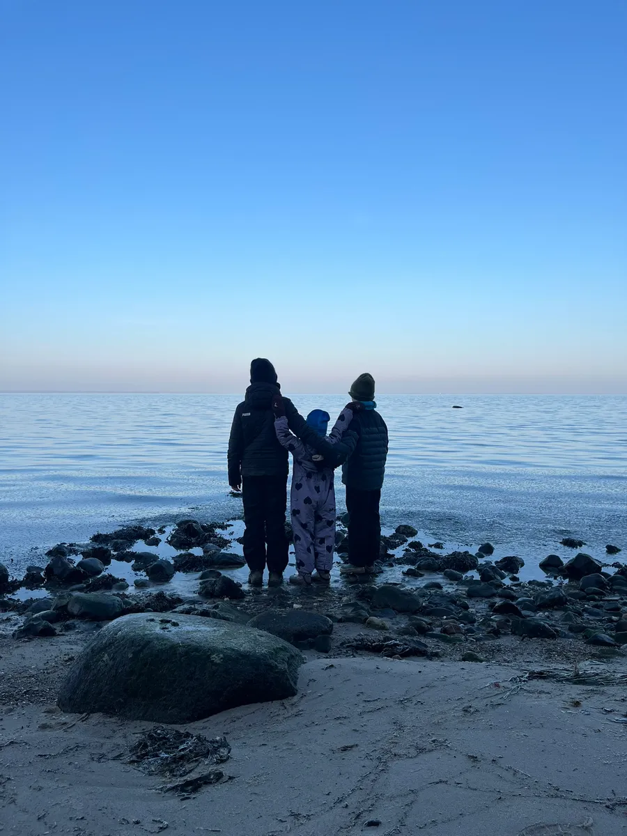 Familiens tre børn står sammen ved vandet